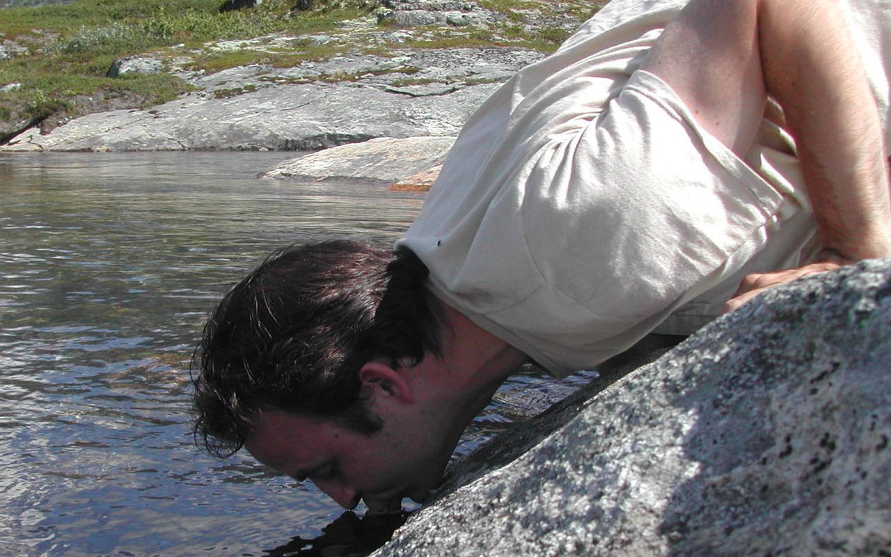 Человек пьет воду из реки